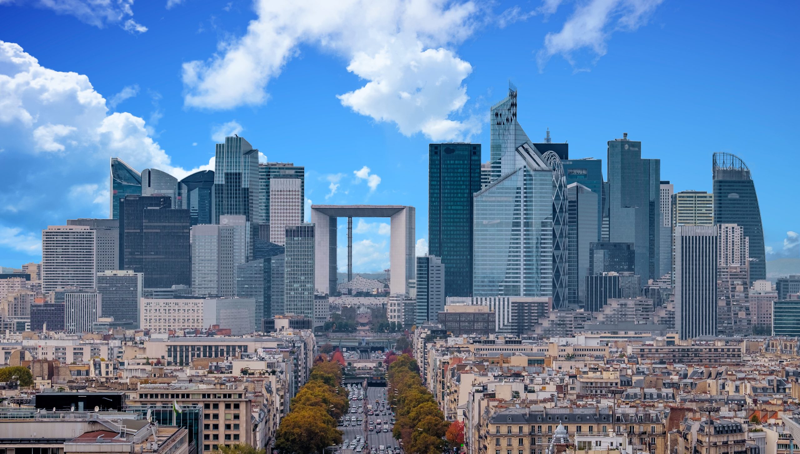 La Defense Financial District Paris France in autumn. Traffic on Champs-Elysees with orange and yellow trees aside. Modern vs. Old architecture. Blue sky with clouds.